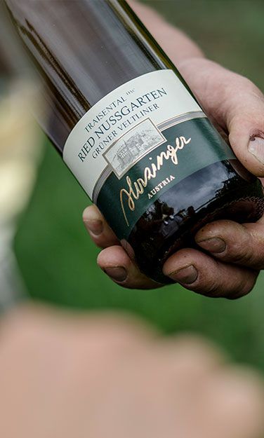 Person die eine Weinflasche von Herzinger hält